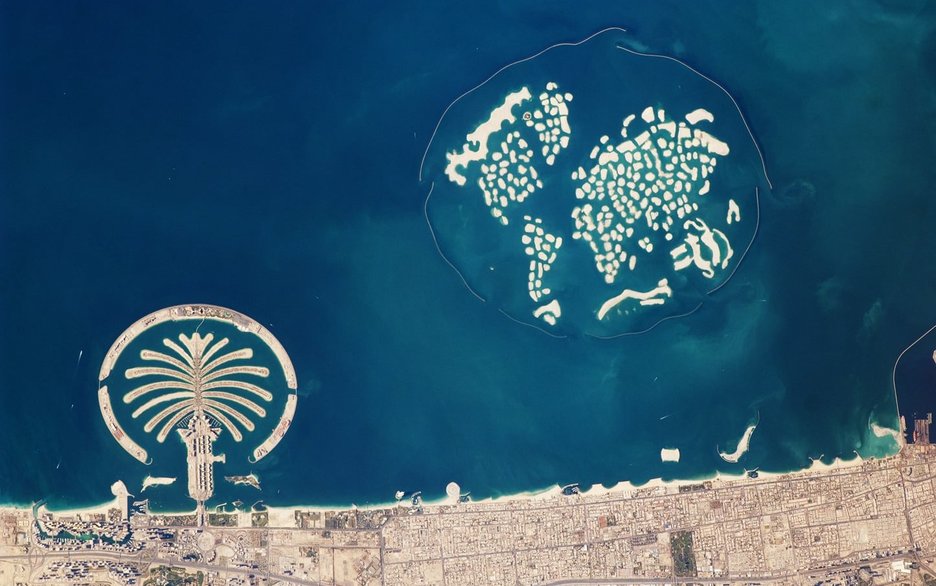 Das Bild ist von einem Satelliten aus dem All aufgenommen. Es zeigt künstlich aufgeschüttete Sandinseln im Persischen Golf, die eine besondere Form haben. Links auf dem Bild ist eine Palme zu sehen, die „The Palm Jumeirah“ genannt wird. Hier leben rund 10.000 Einwohner. Rechts sind 300 Inseln zu sehen, die so angeordnet wurden, dass sie die Kontinente der Welt abbilden. Diese künstliche Insellandschaft heißt „The World“ und ist bisher unbewohnt. Link zur vergrößerten Darstellung des Bildes.