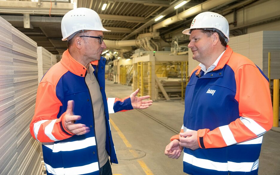 Das Bild zeigt den Werksleiter Thomas Kroiher und die Sicherheitsfachkraft Manfred Kaiser im Gespräch vor Ort in der Produktionshalle von Knauf Intergral Satteldorf. Link zum Artikel.
