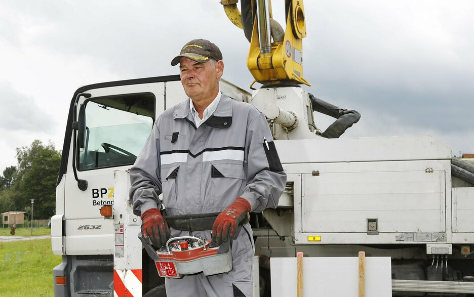 Das Bild zeigt den Betonpumpenmaschinisten Josef Schips bei der Arbeit an der Betonpumpe. Er trägt eine Fernbedienung um den Bauch.  Link zum Artikel.