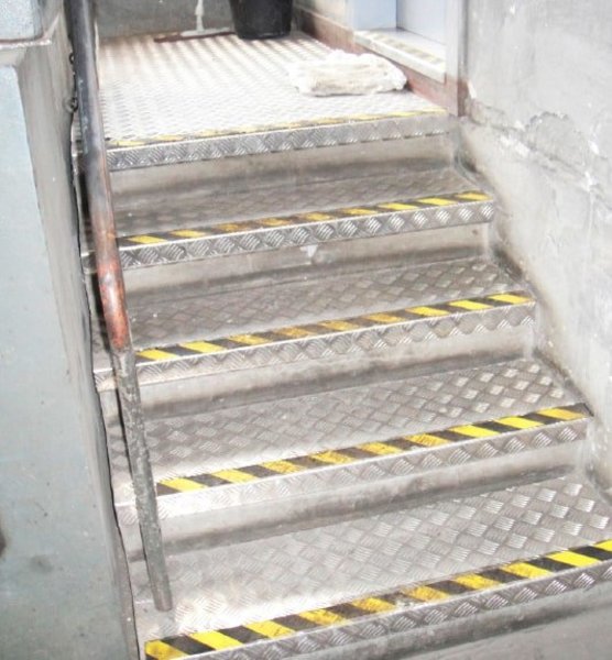 Zu sehen ist eine Treppe, die mit neuen Riffelblechen und einer gelb-schwarzen Gefahrenkennzeichnung an den Stufen ausgestattet wurde.