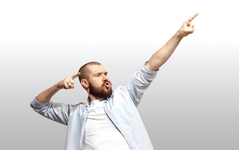 Ein Mann mit Bart, Hemd und T-Shirt macht eine große Geste, so, als wolle er einen Pfeil in die Zukunft abschießen. Dabei weisen die Zeigefinger seiner Hände nach vorn. Dieses Symbolfoto wird genutzt für den Selbst-Check, um die Zielorientierung auf sich selbst zu verdeutlichen. Link zum Artikel.