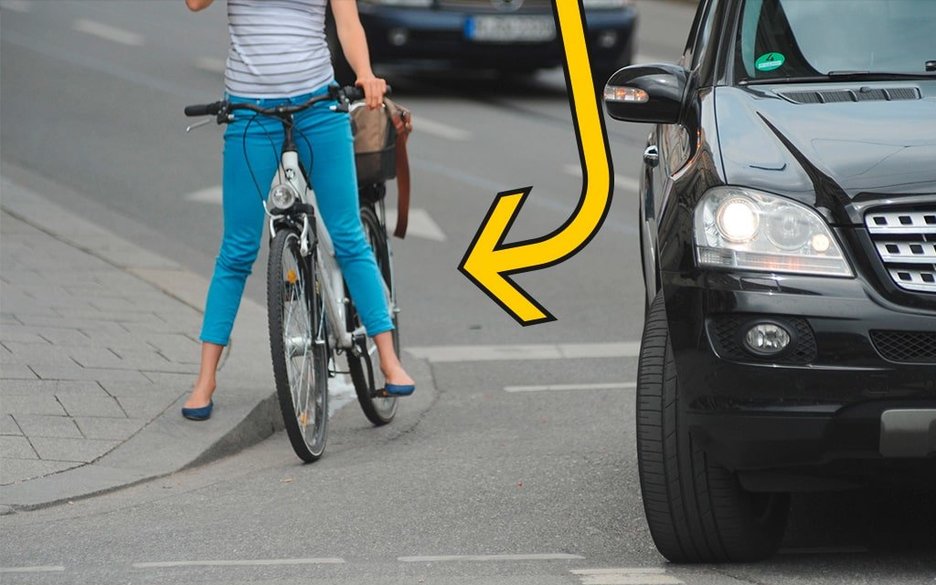 An einer Kreuzung befindet sich ein rechtsabbiegender Pkw. Rechts daneben wartet eine Radfahrerin auf der Straße ab, was passiert. Link zum Artikel.