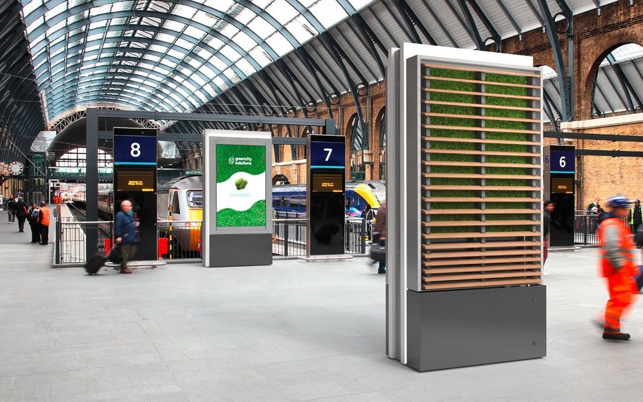 Das Bild zeigt zwei CityTrees in einem Bahnhofsgebäude in Form von Stelen. Auf der einen Seite der CityTrees befindet sich eine grüne, luftreinigende Mooswand, auf der anderen ein 75-Zoll-LCD-Bildschirm. Link zur vergrößerten Darstellung des Bildes.