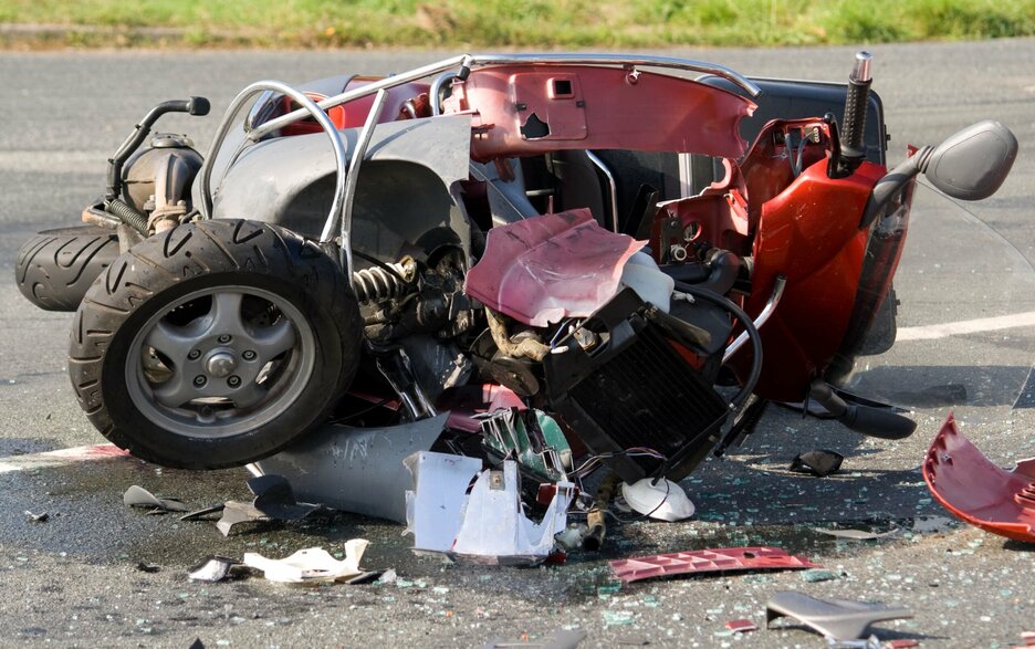 Das Bild zeigt einen zerstörten roten Motorroller, der auf der Straße liegt. Dieses steht symbolhaft für das Übersehen werden von Motorrad-, Mofa- und Rollerfahrern durch Autofahrer. Link zum Artikel.