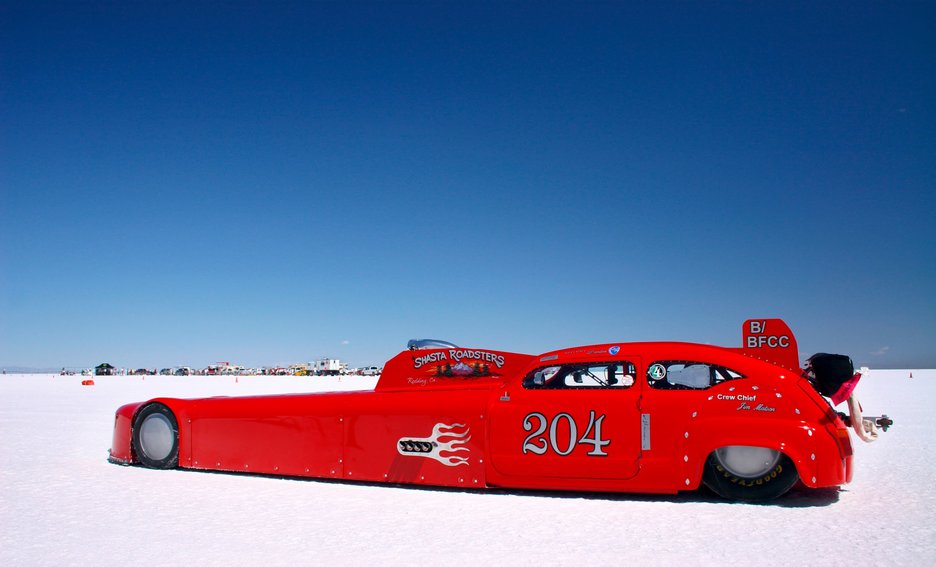 Das Bild zeigt ein extrem langes, rotes Rennauto mit sehr speziellem Design. Solche Fahrzeuge werden extra gebaut für Hochgeschwindigkeitsfahrten in der Salzwüste im Westen der USA.  Link zur vergrößerten Darstellung des Bildes.