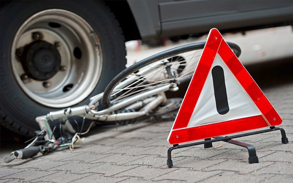 Zu sehen ist ein verunfalltes Fahrrad, auf dem ein Autoreifen steht. Davor ist ein Warndreieck an der Unfallstelle aufgebaut. Link zum Artikel.