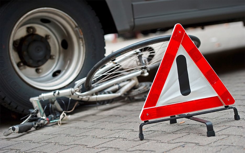 Zu sehen ist ein verunfalltes Fahrrad, auf dem ein Autoreifen steht. Davor ist ein Warndreieck an der Unfallstelle aufgebaut. Link zur vergrößerten Darstellung des Bildes.