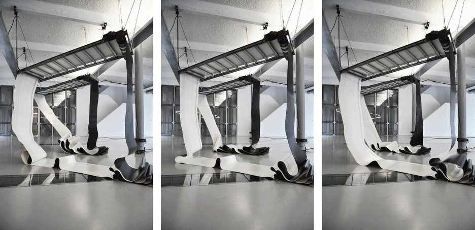 Zu sehen ist eine Bewegungsskulptur des Künstlers Zoro Feigl, die aus auf und ab tanzenden Gurten zweier Förderbänder besteht. Link zur vergrößerten Darstellung des Bildes.