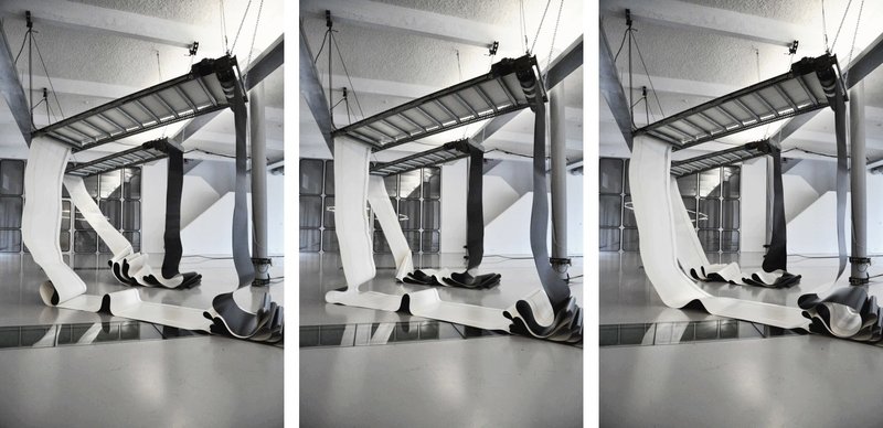 Zu sehen ist eine Bewegungsskulptur des Künstlers Zoro Feigl, die aus auf und ab tanzenden Gurten zweier Förderbänder besteht.