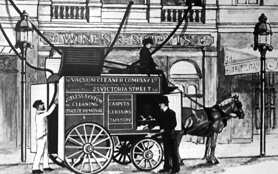 Die Schwarz-Weiß-Zeichnung zeigt einen Pferdekarren beladen mit der motorisierten Saugpumpe von Hubert Cecil Booth vor einem Haus. Vom aufgeklappten Dach des Riesen-Saugers gehen Schläuche über die Fenster in das Haus hinein.  Link zum Artikel.