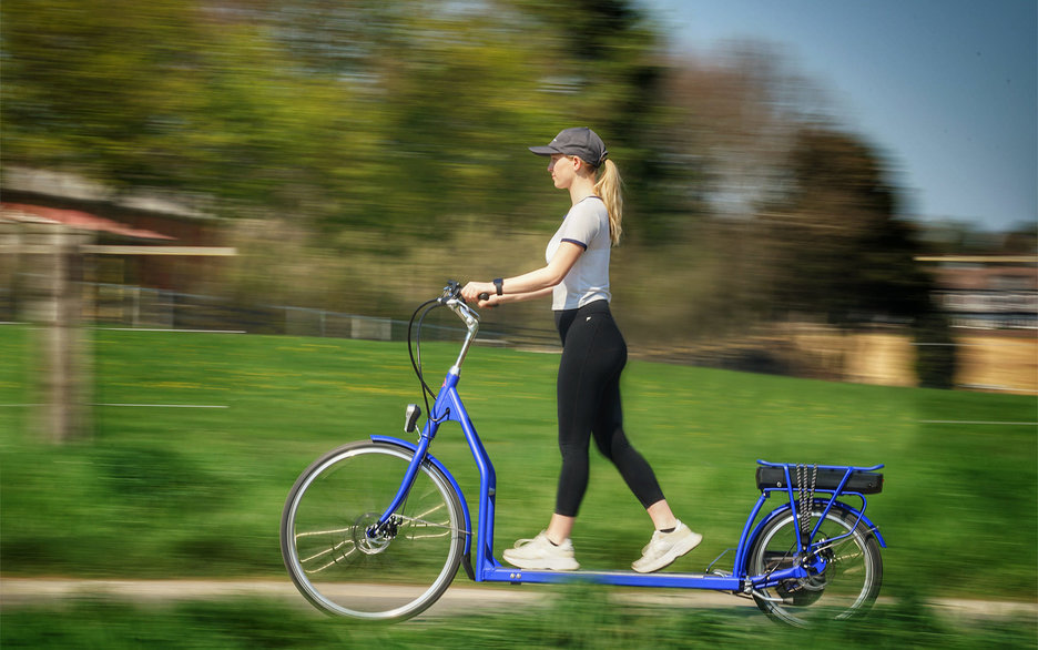 Zu sehen ist eine junge Frau auf einem langen blauen Fahrrad. Sie läuft in der Mitte des Rades mit den Füßen vor und zurück, denn hier befindet sich ein Laufband, welches das Fahrrad antreibt. Link zum Artikel.