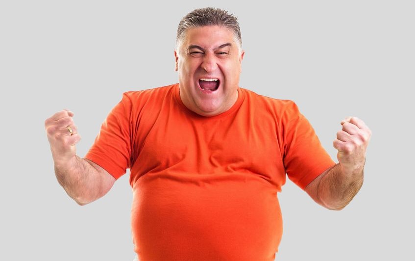 Zu sehen ist ein kräftiger Mann im orangefarbenem T-Shirt, der seine Fäuste ballt und kraftvoll schreit. Dies Symbolfoto für den Selbst-Check Zufriedenheit im Job soll die Kraft verdeutlichen, die entsteht, wenn alles super läuft im Job. Link zur vergrößerten Darstellung des Bildes.