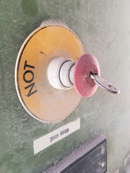 Zu sehen ist ein verbogener Schlüssel an einem Nothalt-Schalter. Er sieht aus, als würde er bald abbrechen.