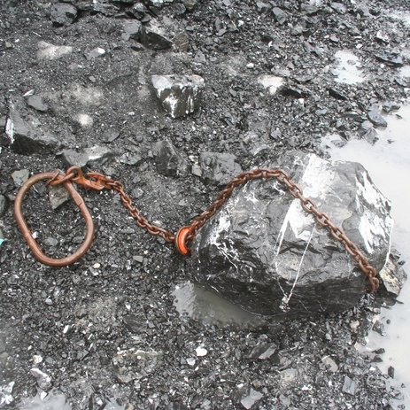 Das Bild zeigt einen großen Gesteinsbrocken, um den eine Anschlagkette mit Haken gezogen wurde.   