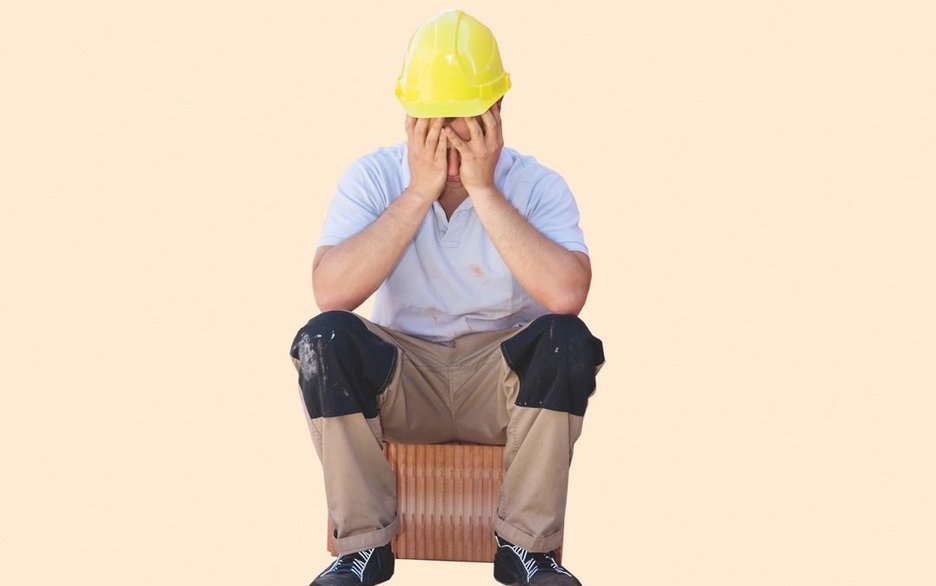 Zu sehen ist ein Mitarbeiter, der auf einen Stein sitzt und seinen Kopf in die Hände stützt. Es scheint ihm nicht gut zu gehen. Dies kann bei Hitzearbeiten passieren. Dann ist schnelle Hilfe gefragt.
