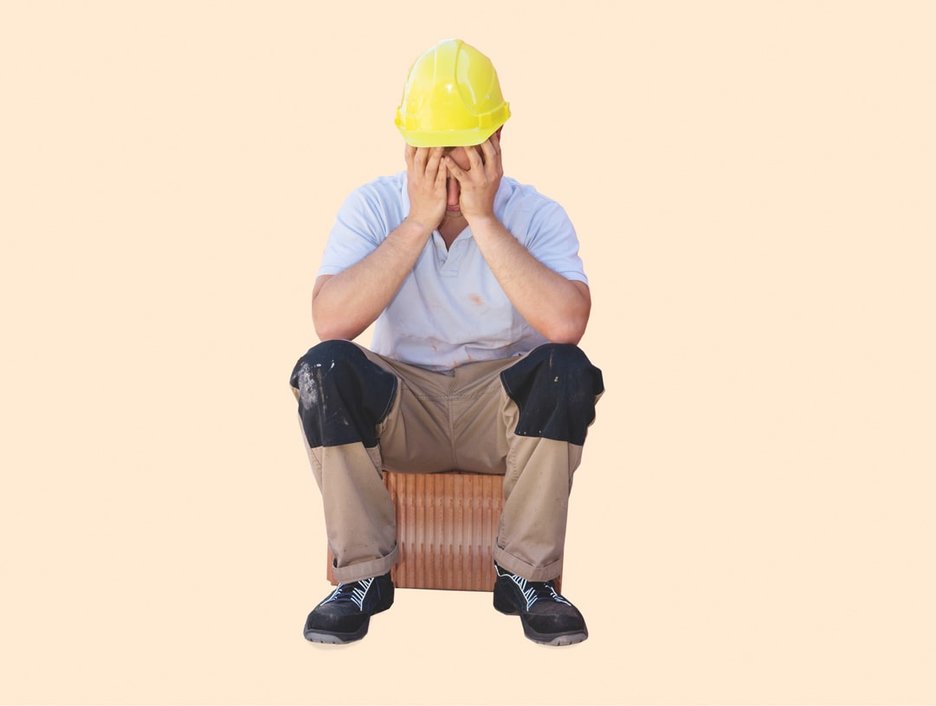 Zu sehen ist ein Mitarbeiter, der auf einen Stein sitzt und seinen Kopf in die Hände stützt. Es scheint ihm nicht gut zu gehen. Dies kann bei Hitzearbeiten passieren. Dann ist schnelle Hilfe gefragt.
