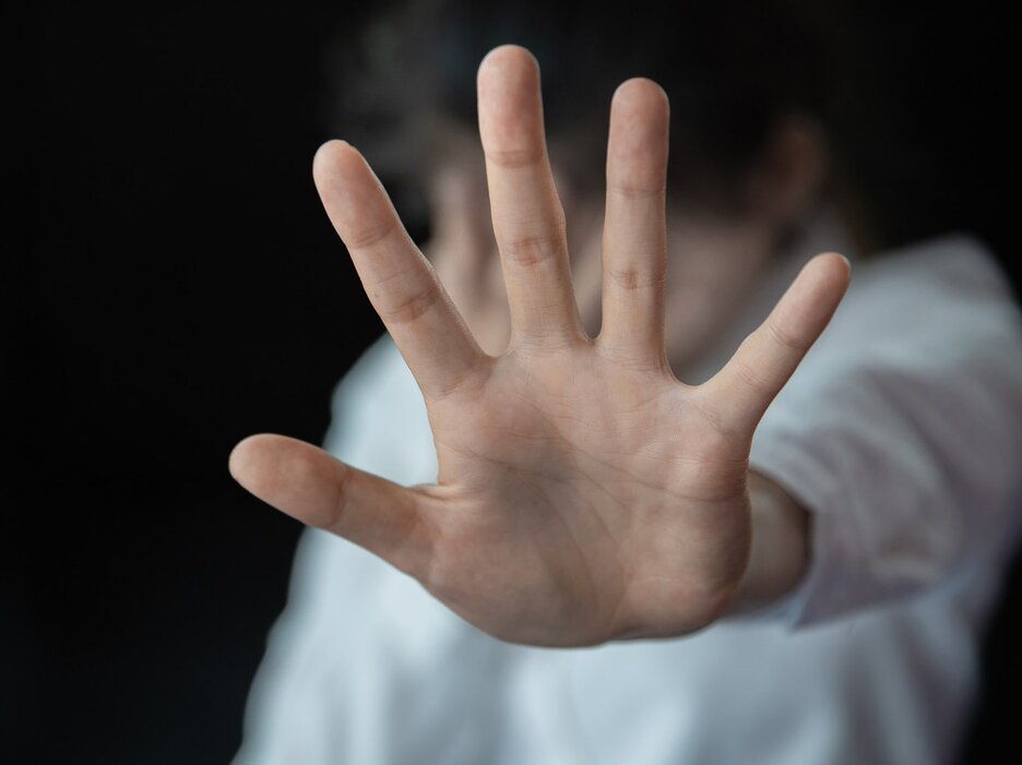 Das Foto ist ein Symbolbild für das Thema „Sexuelle Belästigung am Arbeitsplatz“ und was man dagegen tun kann. Zu sehen ist die Hand einer Frau, die sich mit abgespreizten Fingern abwehrend nach vorne bewegt. Der Hintergrund ist unscharf. Link zur vergrößerten Darstellung des Bildes.
