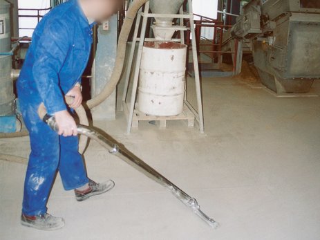 Zu sehen ist ein Mitarbeiter in einer Produktionshalle, der den entstandenen Staub vom Boden absaugt. Link zur vergrößerten Darstellung des Bildes.