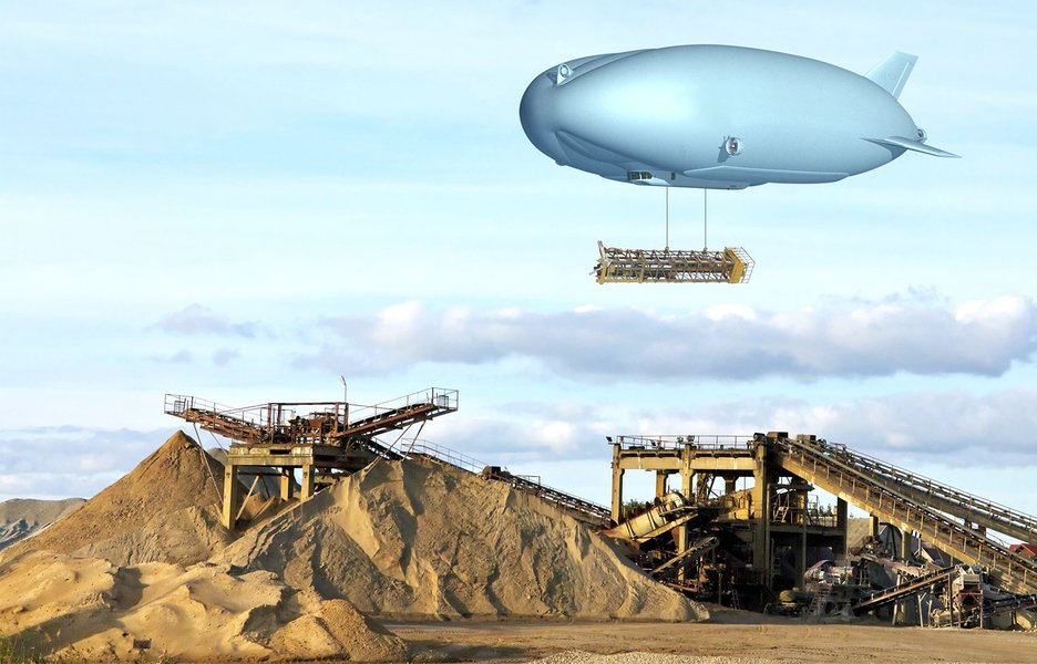 Das Bild zeigt einen Zeppelin, unter dem eine große Last hängt. Dieser schwebt über einer Baustelle in unwegsamem Gelände, an der gerade eine Brücke entsteht. Der Lasten-Zeppelin kann Teile mit bis zu neunzig Tonnen Gewicht heben.