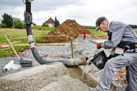 Das Bild zeigt den Betonpumpenmaschinisten Josef Schips, der zur Reinigung der Betonpumpe Wasser in die Schlauchleitung gießt. Link zur vergrößerten Darstellung des Bildes.