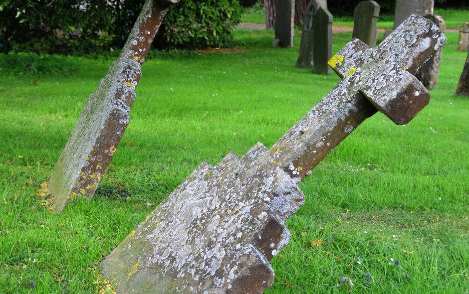 Das Bild zeigt einen schräg stehenden Grabstein, der umzukippen droht und einer Sicherheitsprüfung nicht mehr Stand hält.