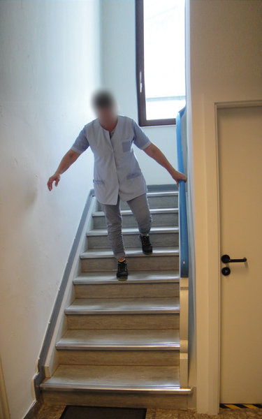 Das Bild zeigt eine nachgestellte Unfallsituation. Zu sehen ist eine Reinigungskraft, wie sie auf den letzten Stufe ins Stolpern gerät, bevor sie die Treppe hinunterstürzt.