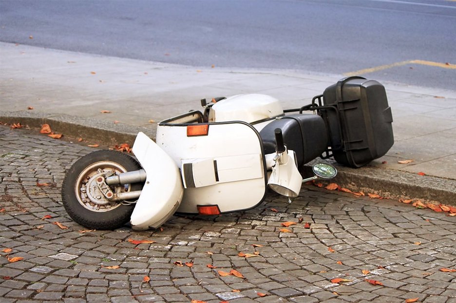 Ein weißer, umgekippter Roller liegt halb auf der Straße und halb auf dem Bürgersteig.