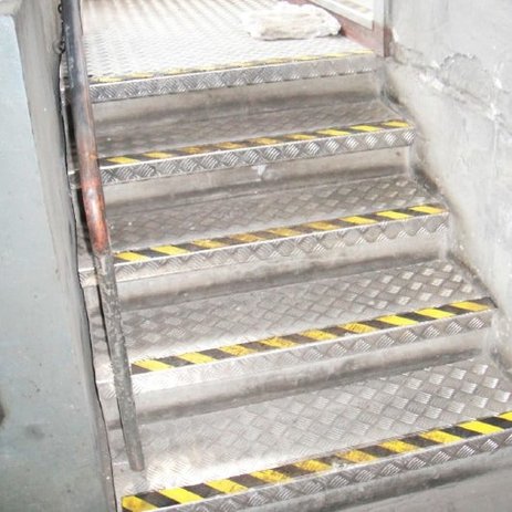 Zu sehen ist eine Treppe, die mit neuen Riffelblechen und einer gelb-schwarzen Gefahrenkennzeichnung an den Stufen ausgestattet wurde.