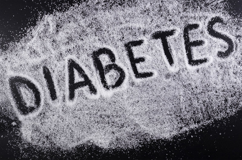 Zu sehen ist eine mit weißem Zucker bestreute schwarze Oberfläche, in die jemand das Wort „Diabetes“ mit dem Finger geschrieben hat.
