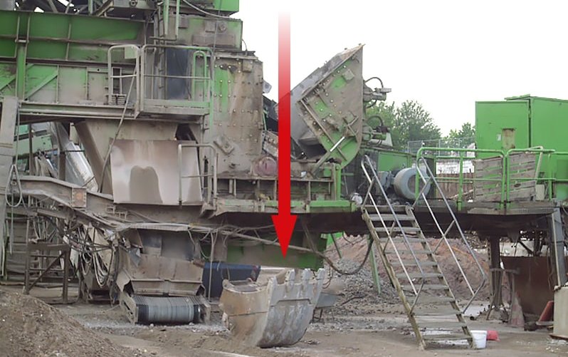 Das Bild zeigt eine Prallmühle, an der gearbeitet wurde und eine abgestürzte Baggerschaufel, die nicht richtig verriegelt war. Ein roter Pfeil weist daraufhin, wo die Schaufel hinunterkrachte.