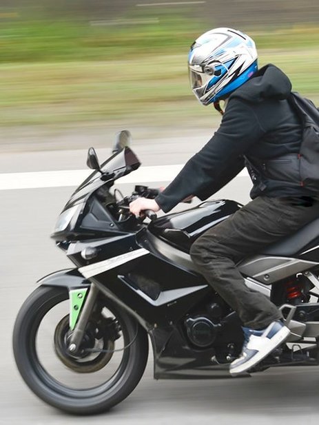 Zu sehen ist ein Motorradfahrer mit Helm während der schnellen Fahrt.