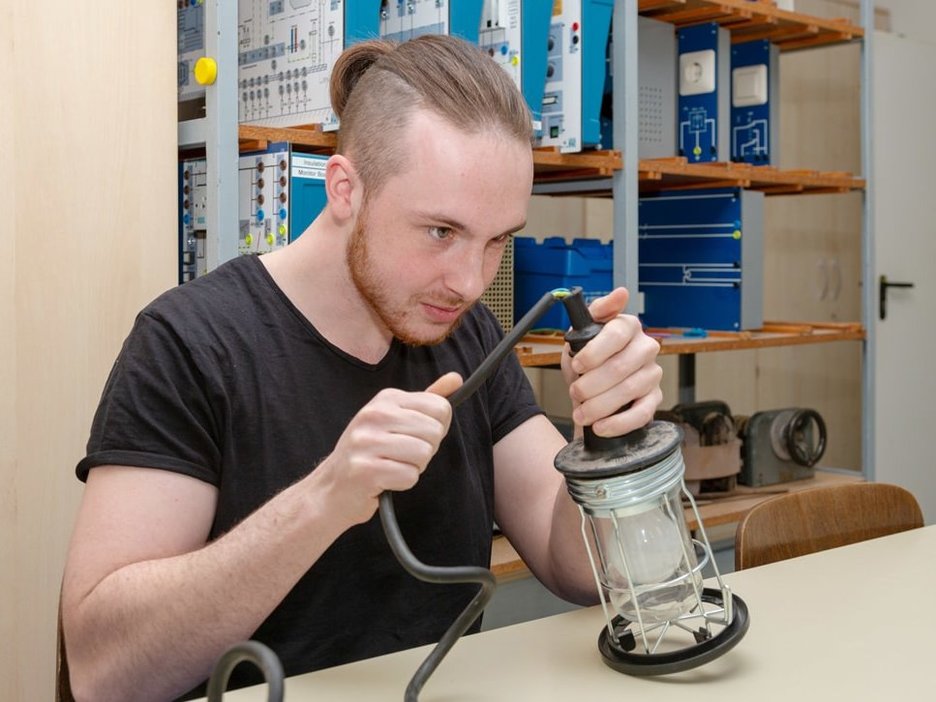 Der Auszubildende zum Chemikanten Joshua Engel macht eine Sicht- und Funktionskontrolle am Kabel einer Elektrolampe. Link zur vergrößerten Darstellung des Bildes.