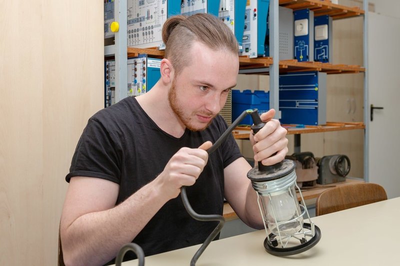 Der Auszubildende zum Chemikanten Joshua Engel macht eine Sicht- und Funktionskontrolle am Kabel einer Elektrolampe.