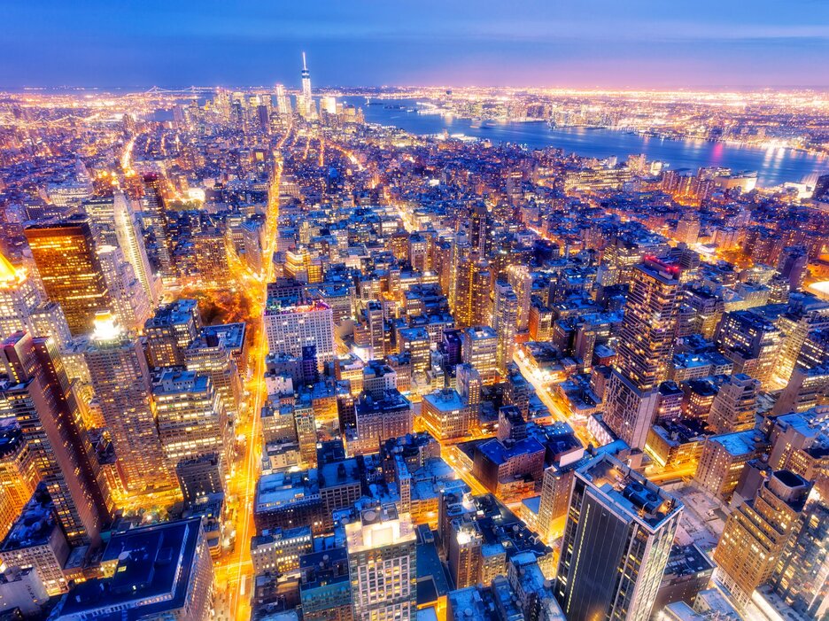 Das Bild aus der Luft zeigt den Blick auf, einen Stadtteil von New York. Zu sehen sind viele künstliche Lichtquellen in und auf den Häusern und die erleuchteten Straßenschluchten, die die Dunkelheit erhellen. Das Bild soll verdeutlichen, wie stark Kunstlicht den Tag-und-Nacht-Rhythmus von Mensch und Natur stört. Link zur vergrößerten Darstellung des Bildes.