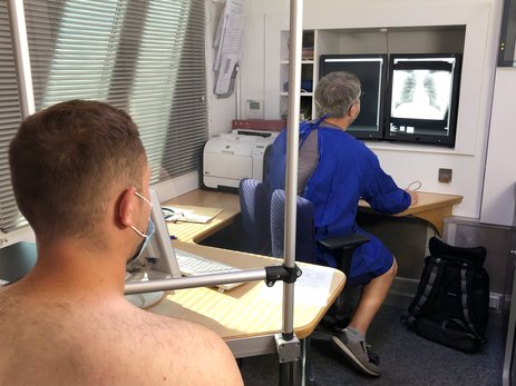 Das Bild zeigt, wie das Röntgenbild der Lunge eines betrieblichen Mitarbeiters von einem Arzt des Röntgenmobils angeschaut und besprochen wird. Beide tragen Corona-Schutzmasken.