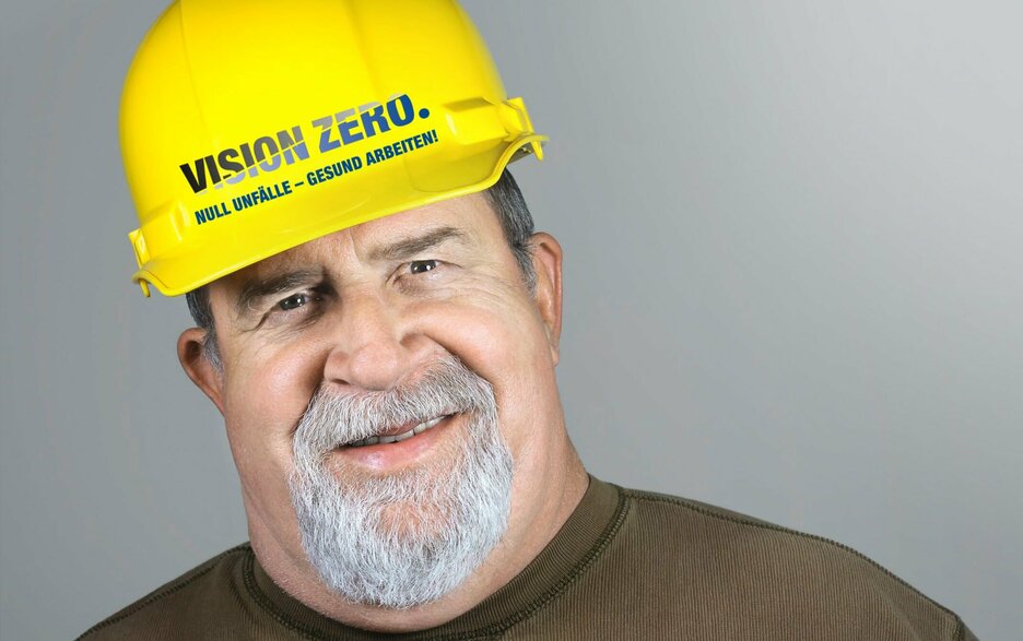 Das Bild zeigt einen lächelnden Bauarbeiter. Auf seinem Helm ist VISION ZERO zu lesen ist. Dieses Zeichen steht für null Unfälle im Betrieb.  Link zum Artikel.
