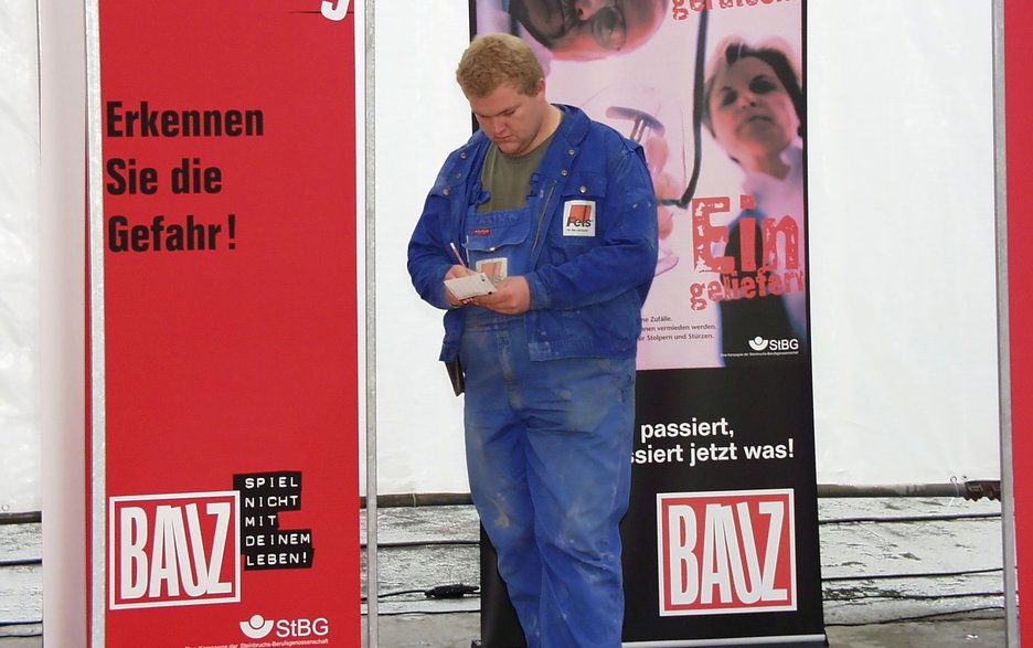Das Bild zeigt einen Mitarbeiter des Betriebes Rüdersdorfer Zement im Jahre 2001 beim Auftaktevent zum Start der BAUZ-Kampagne. Er begeht gerade den BAUZ Stolperparcours und macht sich Notizen bezüglich der eingebauten Stolperfallen. Link zur vergrößerten Darstellung des Bildes.