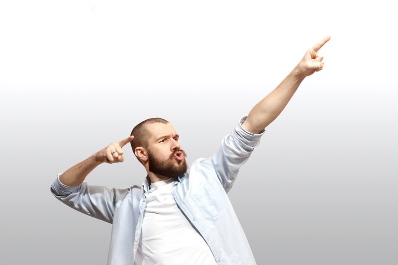 Ein Mann mit Bart, Hemd und T-Shirt macht eine große Geste, so, als wolle er einen Pfeil in die Zukunft abschießen. Dabei weisen die Zeigefinger seiner Hände nach vorn. Dieses Symbolfoto wird genutzt für den Selbst-Check, um die Zielorientierung auf sich selbst zu verdeutlichen.