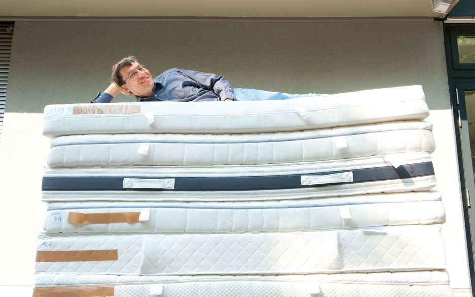 Das Bild zeigt den Matratzentester Peter Brix von der Stiftung Warentest, der gemütlich oben auf einem großen Stapel Matratzen liegt. Link zum Artikel.