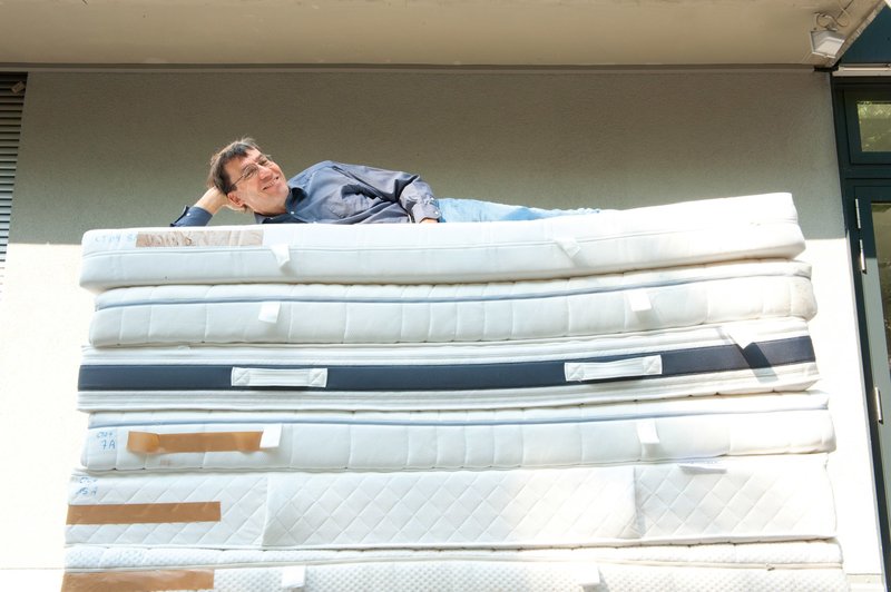 Das Bild zeigt den Matratzentester Peter Brix von der Stiftung Warentest, der gemütlich oben auf einem großen Stapel Matratzen liegt.