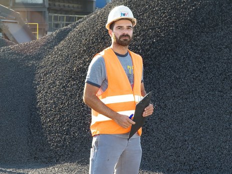 Das Bild zeigt den Betriebsleiter Metin Ayanoglu der Hanseatischen Recyclingprodukt-Vertriebsgesellschaft mbH mit einer Checkliste in der Hand vor einem Materialhaufen. Link zur vergrößerten Darstellung des Bildes.