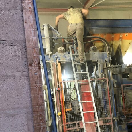 Zu sehen ist ein Mitarbeiter von hinten, der von einer unsicher aufgestellten Anlegeleiter versucht, auf eine hoch gelegene Anlage zu übersteigen. Das ist extrem riskant. Link zur vergrößerten Darstellung des Bildes.