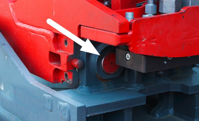 Das Bild zeigt die sichere Verriegelung eines Anbaugerätes einer Erdbaumaschine. Im Detail zu sehen sind die Bolzen, wie sie sicher in der Aufnahmeklaue sitzen. Ein weißer Pfeil zeigt die genaue Stelle an.