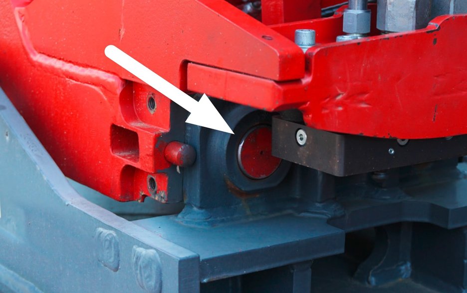 Das Bild zeigt die sichere Verriegelung eines Anbaugerätes einer Erdbaumaschine. Im Detail zu sehen sind die Bolzen, wie sie sicher in der Aufnahmeklaue sitzen. Ein weißer Pfeil zeigt die genaue Stelle an.