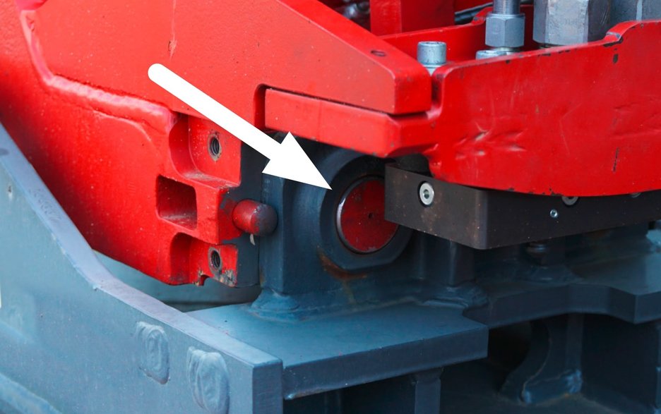 Das Bild zeigt die sichere Verriegelung eines Anbaugerätes einer Erdbaumaschine. Im Detail zu sehen sind die Bolzen, wie sie sicher in der Aufnahmeklaue sitzen. Ein weißer Pfeil zeigt die genaue Stelle an. Link zum Artikel.