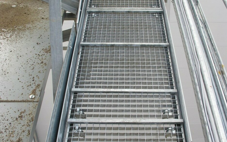 Das Bild zeigt eine Laufbühne von oben, deren Gitterroste zu allen vier Ecken formschlüssig mit Klemmen gesichert sind. Link zum Artikel.