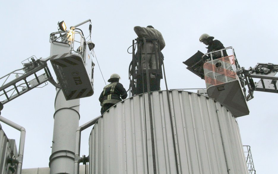 Das Bild zeigt Höhenretter der Feuerwehr, die von Drehleitern aus zwei verunfallte Mitarbeiter von oben aus dem Silo bergen. Link zur vergrößerten Darstellung des Bildes.