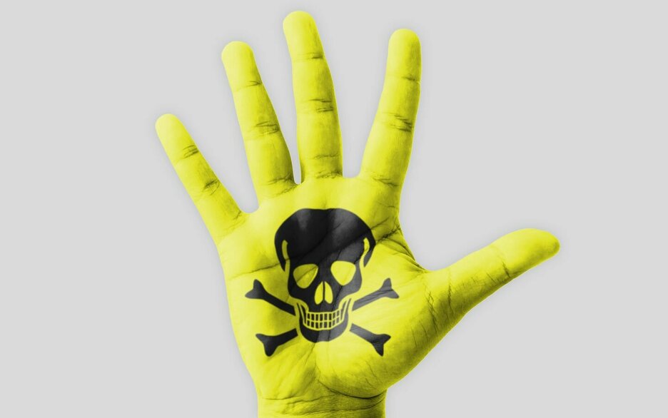 Das Foto zeigt eine Bildmontage. Zu sehen ist eine neongelb eingefärbte Hand, mit einem schwarzen Totenkopf auf der Handinnenfläche. Dies symbolisiert den Umgang mit Gefahrstoffen und die Gefahr, die dabei für die Haut entsteht. Link zum Artikel.