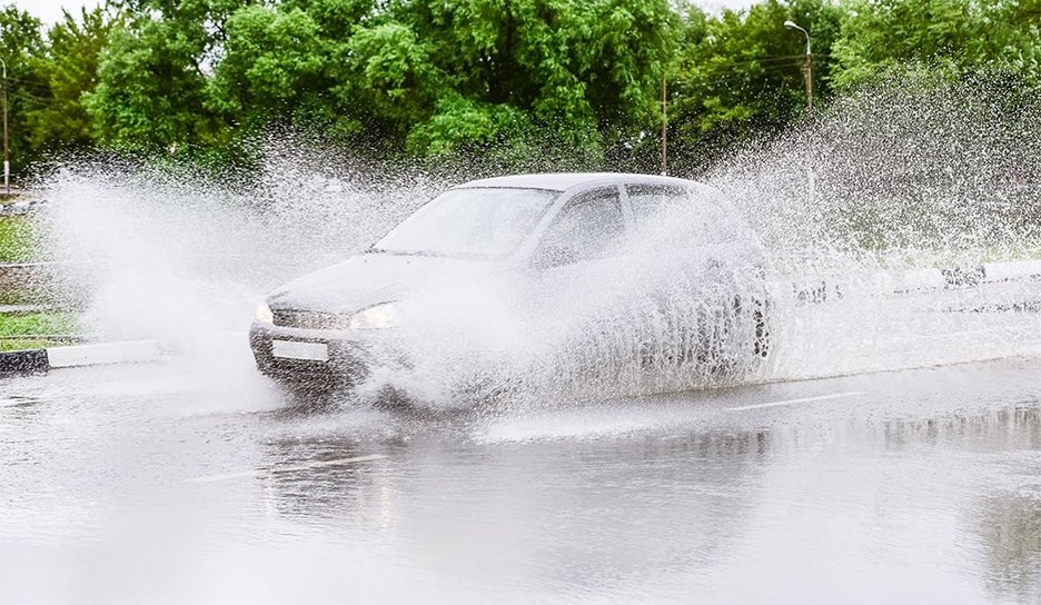 Zu sehen ist ein Auto, das bei Starkregen fährt und in einen Zustand von Aquaplaning gerät.