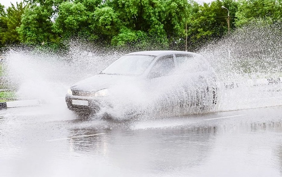 Zu sehen ist ein Auto, das bei Starkregen fährt und in einen Zustand von Aquaplaning gerät.